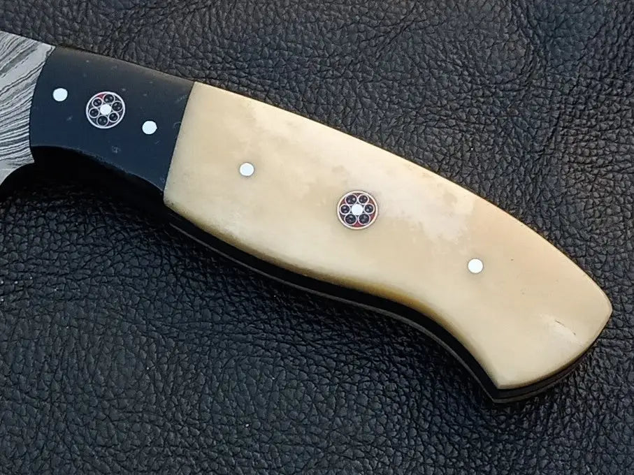 Damascus steel skinning knife with black handle on leather surface.
