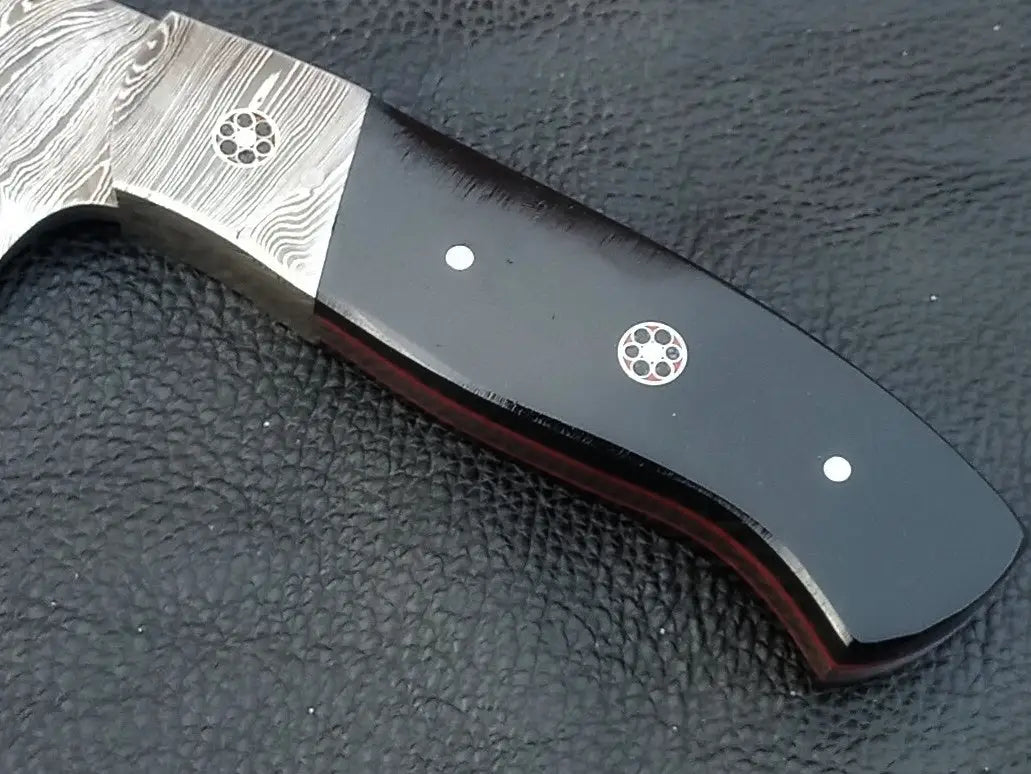 Damascus steel skinner knife with black handle on black surface