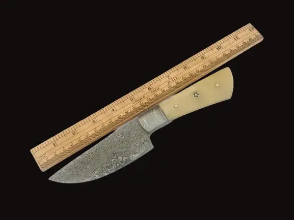 Handmade Damascus steel hunting knife and ruler on white surface