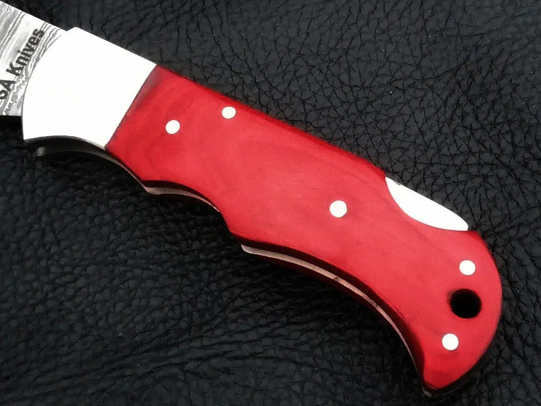 Damascus steel folding knife with red handle on black background