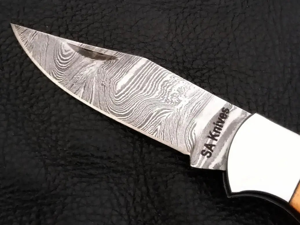 Damascus steel folding knife on black surface with wooden handle