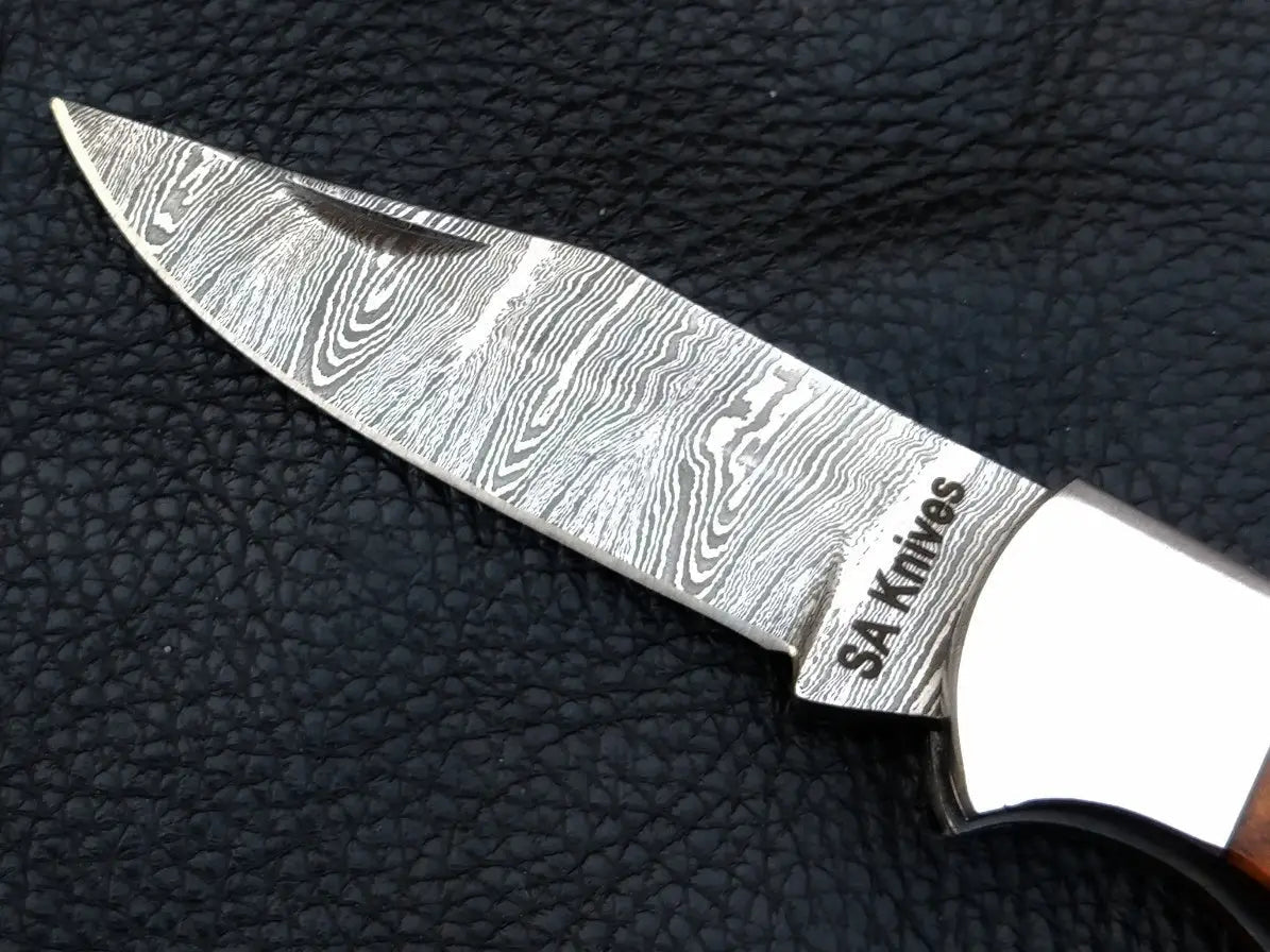 Damascus steel folding knife on leather surface and black background