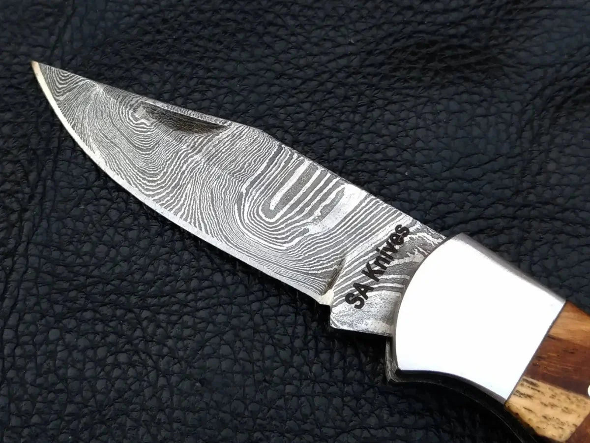 Handmade Damascus steel folding knife on leather surface