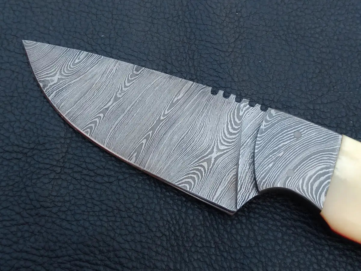 Handmade Damascus steel skinning knife with wooden handle on black leather surface.